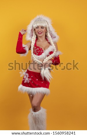 Beautiful emotional young girl dressed as Santa Claus and with long braids hairstyle posing on a yellow background