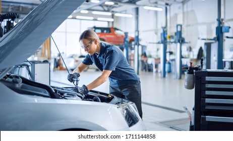 Beautiful Empowering Female Mechanic Is Working On A Car In A Car Service. Woman In Safety Glasses Is Working On An Usual Car Maintenance. She's Using A Ratchet. Modern Clean Workshop With Cars.