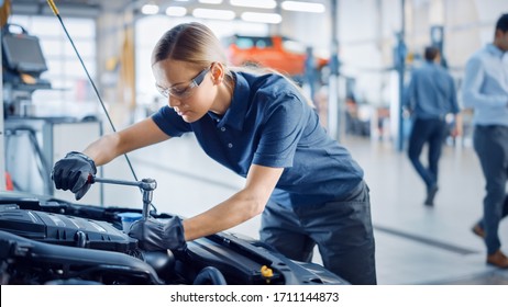 Beautiful Empowering Female Mechanic is Working on a Car in a Car Service. Woman in Safety Glasses is Working on an Usual Car Maintenance. She's Using a Ratchet. Modern Clean Workshop with Cars. - Powered by Shutterstock