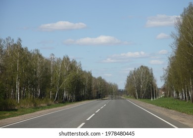 Beautiful Endless Empty Asphalted Two Way Highway Road With Birch Trees Forest On Roadsides Perspective View From Car, European Travel Landscape At Sunny Spring Day On Blue Sky Background