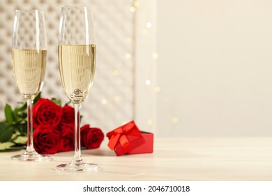 Beautiful Engagement Ring With Gemstone In Glass Of Sparkling Wine And Roses On White Wooden Table. Space For Text