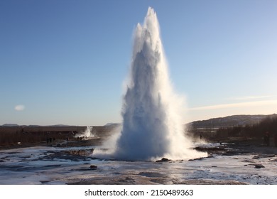 Beautiful eruption of a big geyser surrounded by ice in the geothermal Geysir park during a sunny spring day in Iceland, Europe