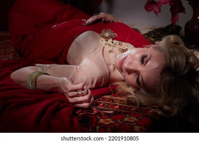 A beautiful European girl looking like an Arab woman in a red room in a harem. Photo shoot of an oriental style odalisque. A model poses in a sari as an indian woman in india
