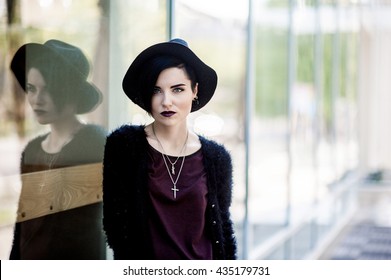 Beautiful european woman with black hair and dark lipstick standing near the large windows and looking at the camera