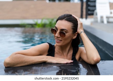 Beautiful European Woman In Black Swimsuit Posing Outside At Villa In Swimming Pool, On Vacation, Perfect Shape, Good Body, Tanned, Fit, Wearing Trendy Brown Sunglasses