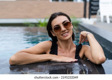 Beautiful European Woman In Black Swimsuit Posing Outside At Villa In Swimming Pool, On Vacation, Perfect Shape, Good Body, Tanned, Fit, Wearing Trendy Brown Sunglasses