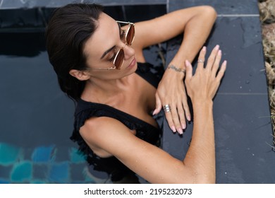 Beautiful European Woman In Black Swimsuit Posing Outside At Villa In Swimming Pool, On Vacation, Perfect Shape, Good Body, Tanned, Fit, Wearing Trendy Brown Sunglasses