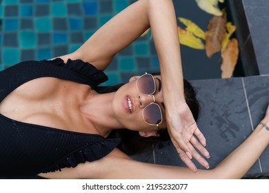 Beautiful European Woman In Black Swimsuit Posing Outside At Villa In Swimming Pool, On Vacation, Perfect Shape, Good Body, Tanned, Fit, Wearing Trendy Brown Sunglasses