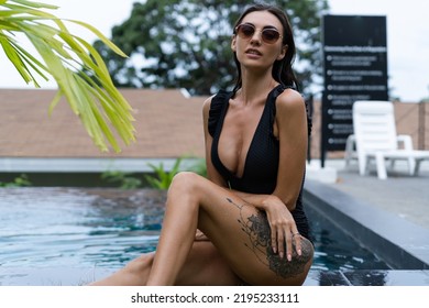 Beautiful European Woman In Black Swimsuit Posing Outside At Villa In Swimming Pool, On Vacation, Perfect Shape, Good Body, Tanned, Fit, Wearing Trendy Brown Sunglasses