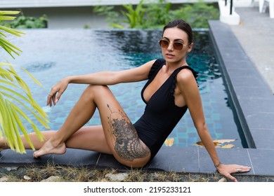 Beautiful European Woman In Black Swimsuit Posing Outside At Villa In Swimming Pool, On Vacation, Perfect Shape, Good Body, Tanned, Fit, Wearing Trendy Brown Sunglasses