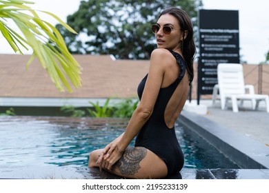 Beautiful European Woman In Black Swimsuit Posing Outside At Villa In Swimming Pool, On Vacation, Perfect Shape, Good Body, Tanned, Fit, Wearing Trendy Brown Sunglasses