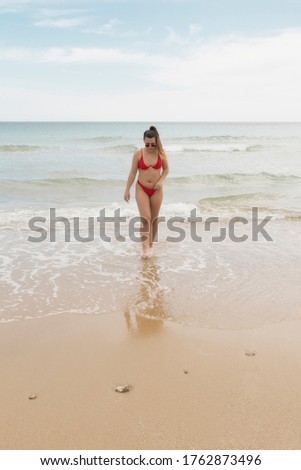 beautiful european young girl in red bikini on th beach. portrait of a woman smiling at the sea. girl in swimwear enjoying and walking on the beach