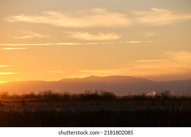 Beautiful evening panoramic landscape with bright setting sun over distant mountain peaks and asphalt road in front at sunset