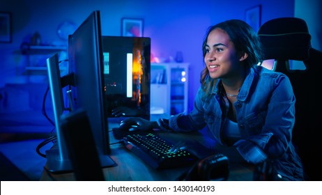 Beautiful and Excited Black Gamer Girl is Playing First-Person Shooter Online Video Game on Her Computer. Room and PC have Blue Neon Led Lights. Cozy Evening at Home.