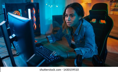 Beautiful And Excited Black Gamer Girl Is Playing Online Video Game On Her Personal Computer. Room And PC Have Colorful Warm Neon Led Lights. Cozy Evening At Home.