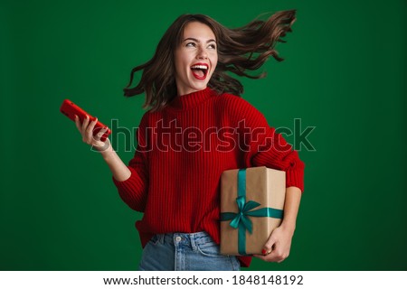 Beautiful excited girl screaming while posing with Christmas gift and cellphone isolated over green background