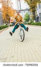 Beautiful Excited Woman In Yellow Coat Riding Bike In Park