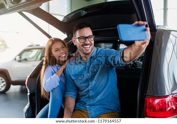 Beautiful excited young couple at car showroom\
taking selfie photo in their new\
car.