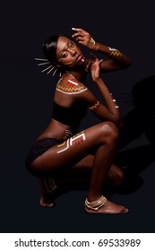 Beautiful Exotic African Female Fashion With Tribal Yellow Red And White Makeup Cosmetics And Sticks In Hair, In Cultural Dance Position.