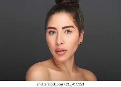 Beautiful exotic model with green eyes in beauty portrait. High fashion beauty and skin shoot in studio of latina or hispanic model with young and fresh skin. Shot on a gray background.