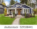 Beautiful exterior of newly built luxury home. Yard with green grass and walkway lead to ornately designed covered porch and front entrance. 