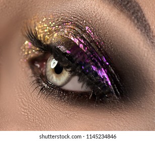 Beautiful Eye Make-up with colorful sparks. Beauty bright fashion holiday smoky eye makeup. Make up sample, close-up of model woman green color eye. Purple and golden glitter eyeshadows