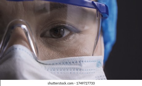 Beautiful Eye Of A Tired Doctor Wearing Safety Glasses. Asian Woman In Protective Glasses And Mask Looking At Camera. Super Close Up Shot.