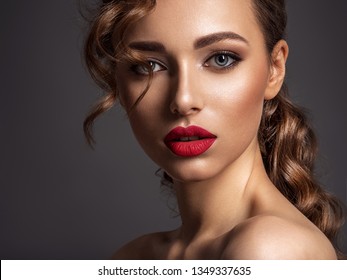 Beautiful face of young woman with red lipstick. Portrait of a stunning sexy girl looks at camera. Attractive model with stylish makeup.  Closeup portrait of a caucasian female. 