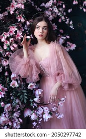 Beautiful fair skinned girl in romatic long pink dress surrounded by magnolia flowers standing in front of old blue door