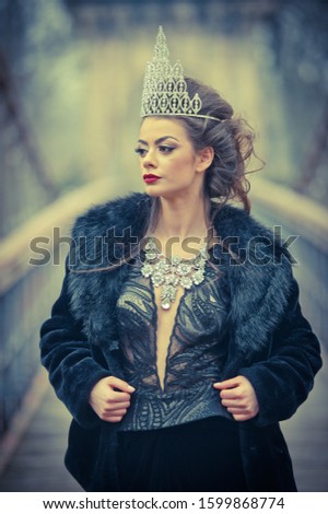 Beautiful fairy-tale winter queen in the forest with sparkling tiara and Elegant black fur coat. Fluffy snow flakes.