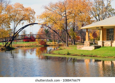 Beautiful Fall Landscape With A Bridge In The City Park. Colored Trees, Bridge And Pavilion In Sunlight Reflected In The Lake Mendota Bay Water. Tenney Park, Madison, Midwest USA, Wisconsin.