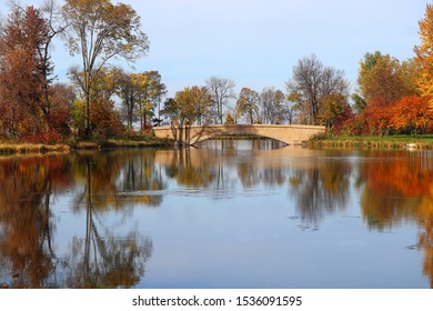 Beautiful Fall Landscape With A Bridge In The City Park.Scenic View With Colored Trees Around Old Style Bridge In Sunlight Reflected In The Lake Mendota Bay Water. Tenney Park, Madison, Wisconsin, USA