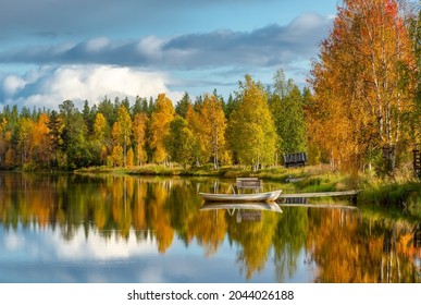 Beautiful fall scenery. Stunning morning view of calm water lake with a reflection of colorful autumn forest. Small wooden boat on the lakeshore at autumn in Finland. Ruska season in Finland. 