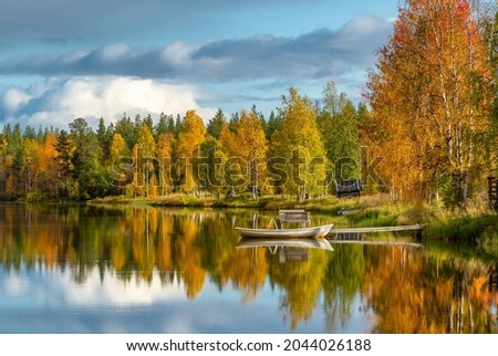 Beautiful fall scenery. Stunning morning view of calm water lake with a reflection of colorful autumn forest. Small wooden boat on the lakeshore at autumn in Finland. Ruska season in Finland. 