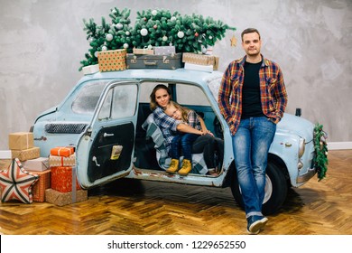 Beautiful Family In Checked Shirts Standing Near Blue Retro Car With Presents On The Roof. Family In Stylish Decorated Interior Studio For Christmas And New Year Holidays