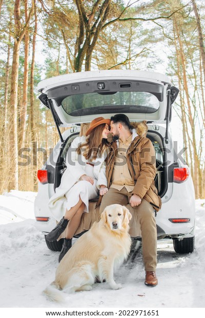 Beautiful family  and cute dog\
sitting in the trunk of a car winter season.\
Vacation.\
Travel.