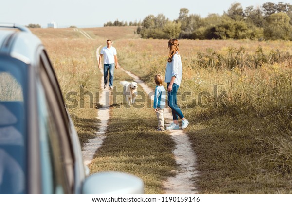 beautiful family with dog walking by field\
road together with car on\
foreground