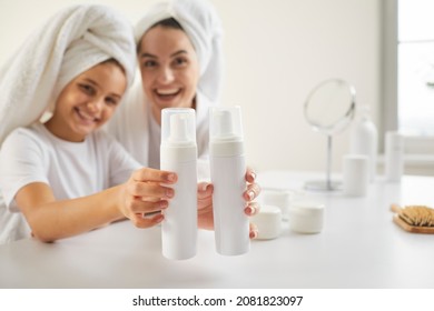 Beautiful Family Doing Morning Hair Care. Smiling Mom And Kid In Bathroom Towels Show Clean Plastic Mockup Shampoo, Conditioner Or Face Wash Bottles. Children And Adults' Dermatology Products Concept