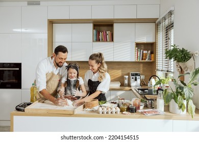 Beautiful family father with beared teaching young daughter kneading dough witn young mother. Delighted kid having fun with parents. - Powered by Shutterstock