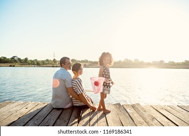 Beautiful Family Fishing In The Lake From The Pier At Sunset