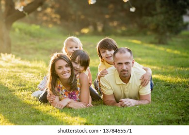 Beautiful Family, Mother, Father And Three Kids, Boys, Having Familly Outdoors Portrait Taken On A Sunny Spring Evening, Beautiful Blooming Garden, Sunset Time, Back Lit. Parents And Children Have Fun