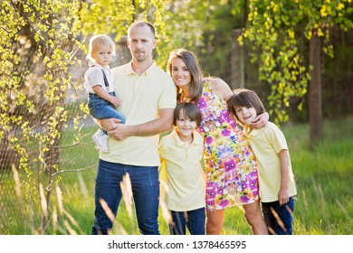 Beautiful Family, Mother, Father And Three Kids, Boys, Having Familly Outdoors Portrait Taken On A Sunny Spring Evening, Beautiful Blooming Garden, Sunset Time, Back Lit. Parents And Children Have Fun