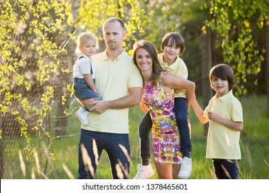 Beautiful Family, Mother, Father And Three Kids, Boys, Having Familly Outdoors Portrait Taken On A Sunny Spring Evening, Beautiful Blooming Garden, Sunset Time, Back Lit. Parents And Children Have Fun