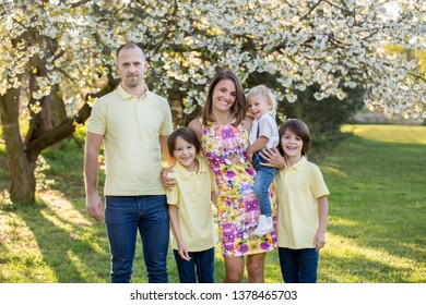 Beautiful Family, Mother, Father And Three Kids, Boys, Having Familly Outdoors Portrait Taken On A Sunny Spring Evening, Beautiful Blooming Garden, Sunset Time, Back Lit. Parents And Children Have Fun