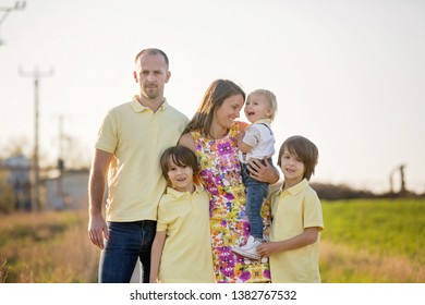 Beautiful Family, Mother, Father And Three Kids, Boys, Having Familly Outdoors Portrait Taken On A Sunny Spring Evening, Beautiful Blooming Garden, Sunset Time, Back Lit. Parents And Children Have Fun