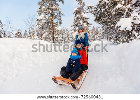 Beautiful family of mother and kids enjoying snowy winter day outdoors having fun sledging