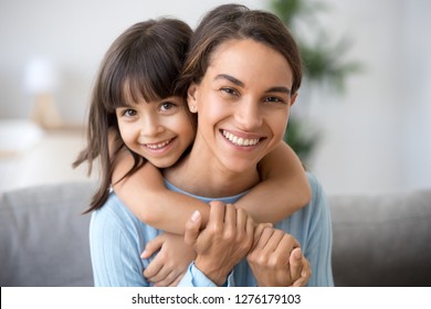 Beautiful Family Of Single Young Mom And Cute Preschool Kid Daughter Embracing Mommy Looking At Camera, Happy Loving Mother Piggybacking Smiling Little Child Girl Hugging Mum Headshot Portrait