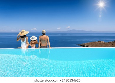 A beautiful family sits by the swimming pool at enjoys the sea view during their summer vacations - Powered by Shutterstock