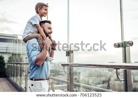 Beautiful family is spending time together  outside. Dad and his little son are having fun on a roof terrace with view on a city. Sitting on father's shoulders and smiling.