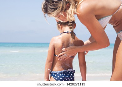 Beautiful Family Visiting Sunny Beach, Mother Applying Uva Sun Protection Cream On Child Back, Covering Skin, Outdoors. Nordic Mom And Child Tourists On Summer Vacation, Leisure Recreation Lifestyle.